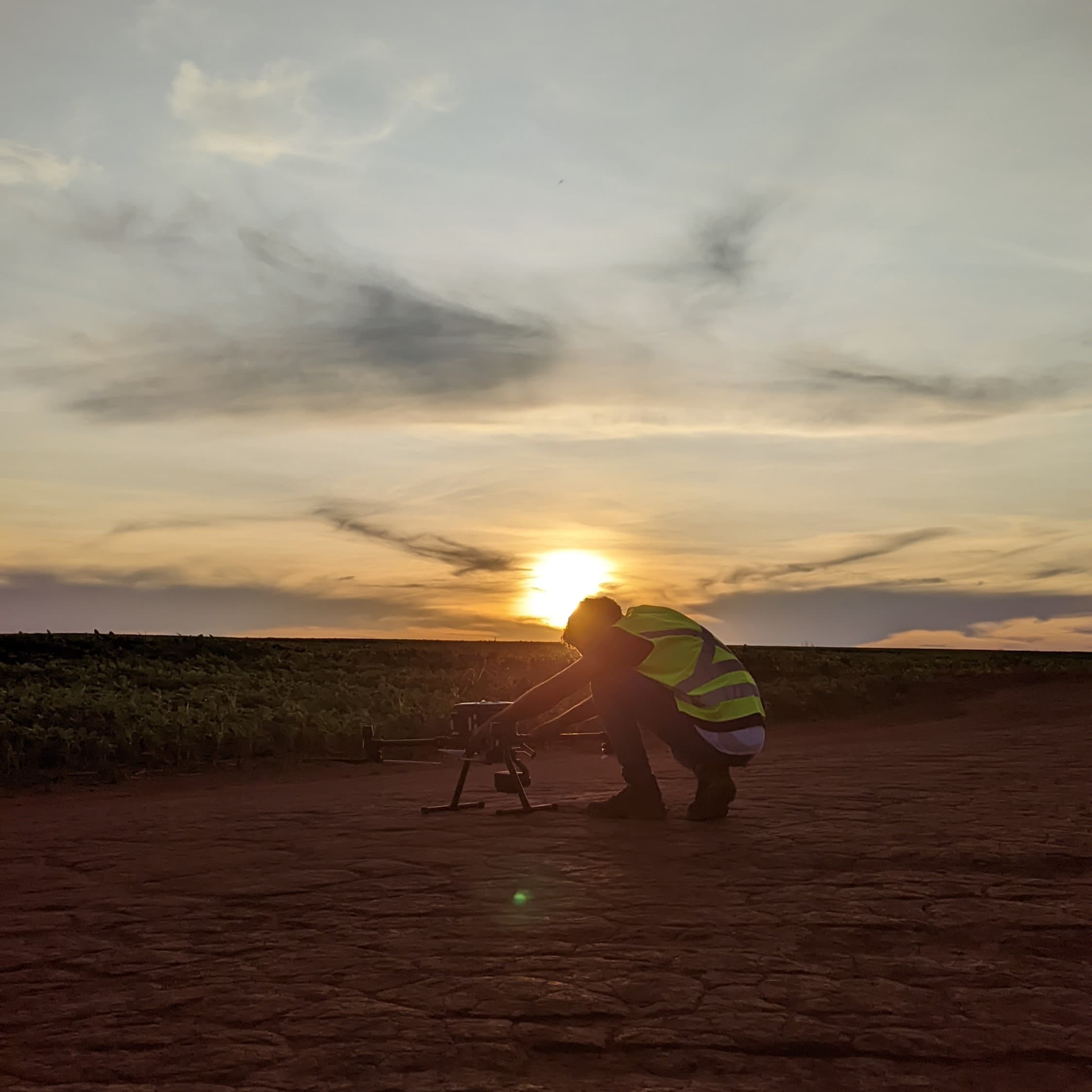 a pilot setting up a drone, backlit by a sunrise